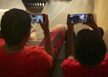 Indian children play online game PUBG on their mobile phones sitting on stairs outside their house  in Hyderabad, India, Friday, April 5, 2019. A boy’s suicide in India after his mother scolded him for playing the popular online game PlayerUnknown’s Battlegrounds has inflamed a debate across the country over whether the game should be banned. (AP Photo/ Mahesh Kumar A.)