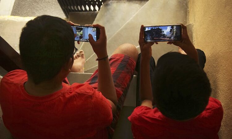 Indian children play online game PUBG on their mobile phones sitting on stairs outside their house  in Hyderabad, India, Friday, April 5, 2019. A boy’s suicide in India after his mother scolded him for playing the popular online game PlayerUnknown’s Battlegrounds has inflamed a debate across the country over whether the game should be banned. (AP Photo/ Mahesh Kumar A.)